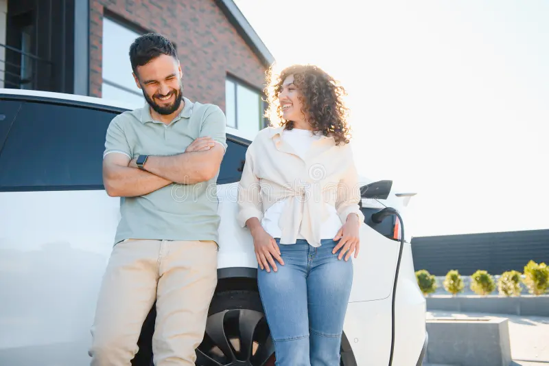 Happy couple leaning against their modern silver sedan